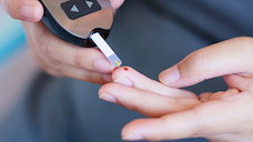 A finger with a small drop of blood after a finger prick